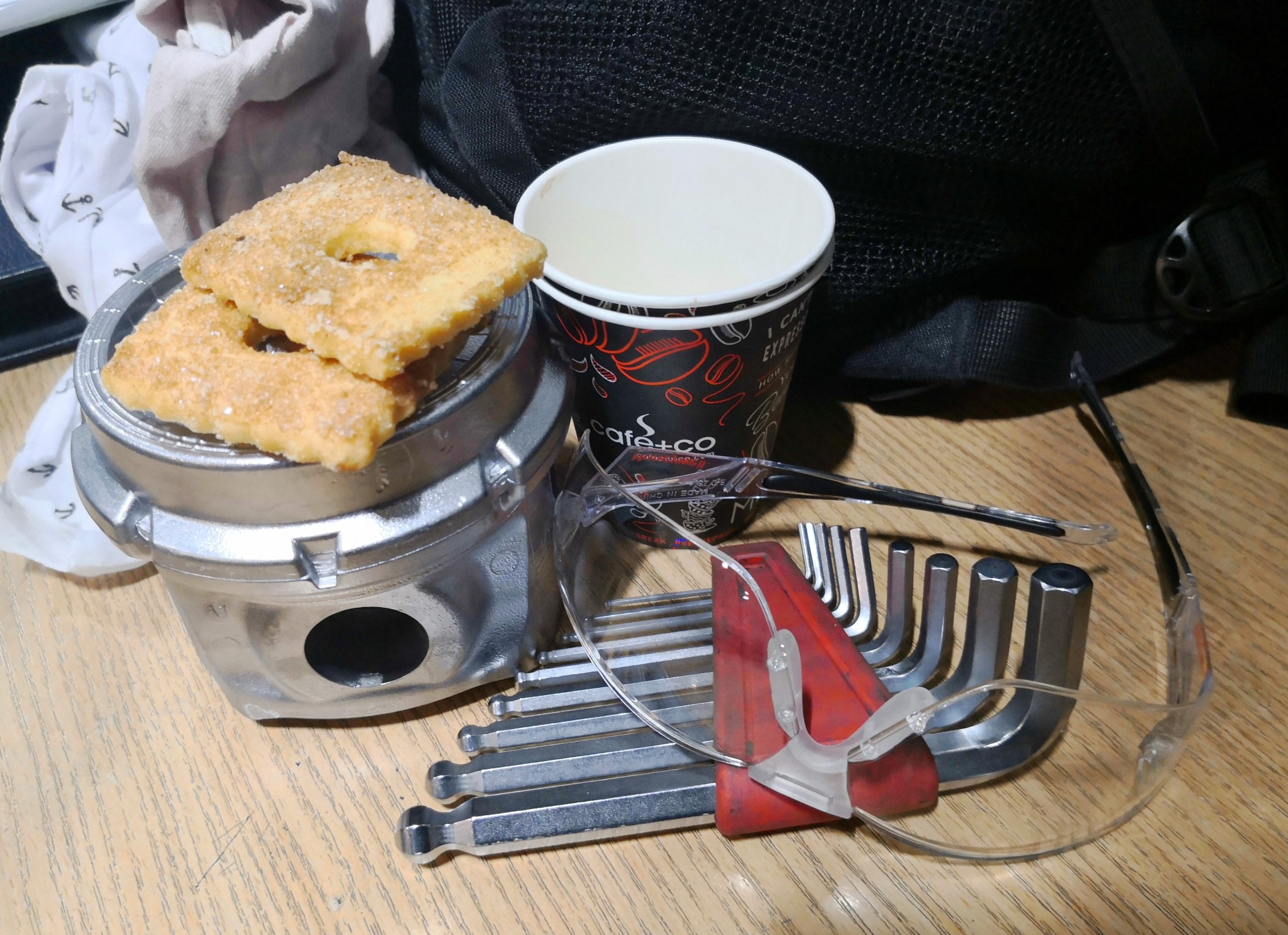 okulary ochronne, kubek na kawę, ciastka leżące na tłoku aluminiowym