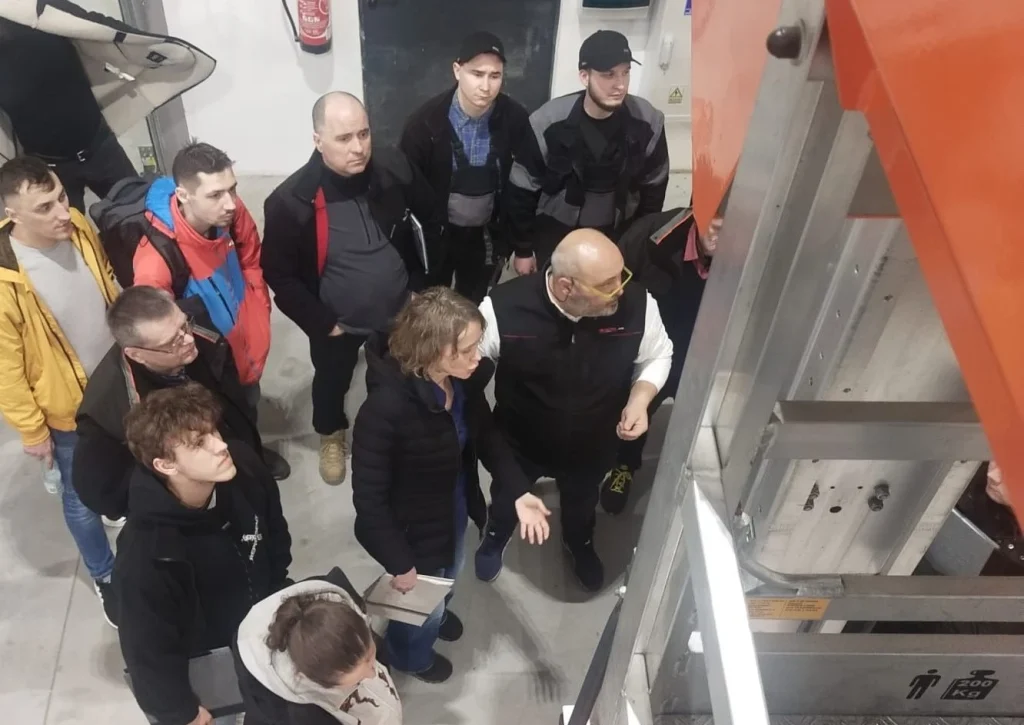 gruppo di persone davanti ad una piattaforma aerea, partecipano ad un corso di formazione in presenza di un traduttore polacco italiano organizzato in Polonia