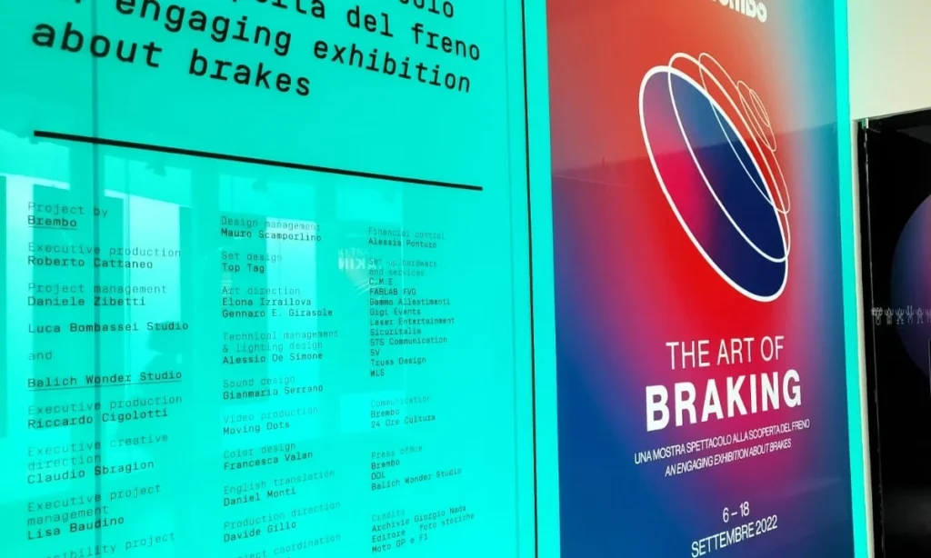 Plansza informacyjna z włoskim tytułem wystawy Brembo „The Art of Braking” przed wejściem do muzeum MUDEC w Mediolanie, związana z włoskim designem i kulturą